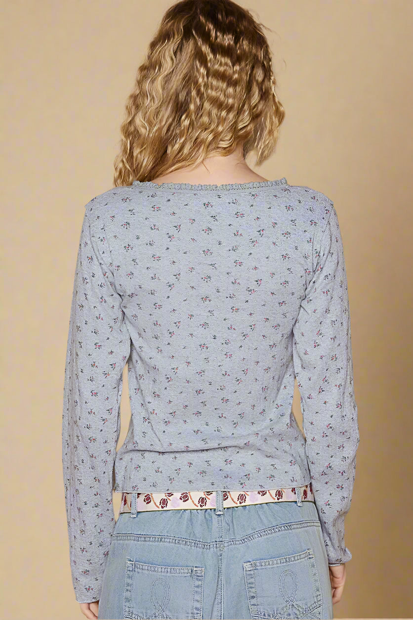 Person wearing a light blue floral long-sleeve top and jeans against a beige background