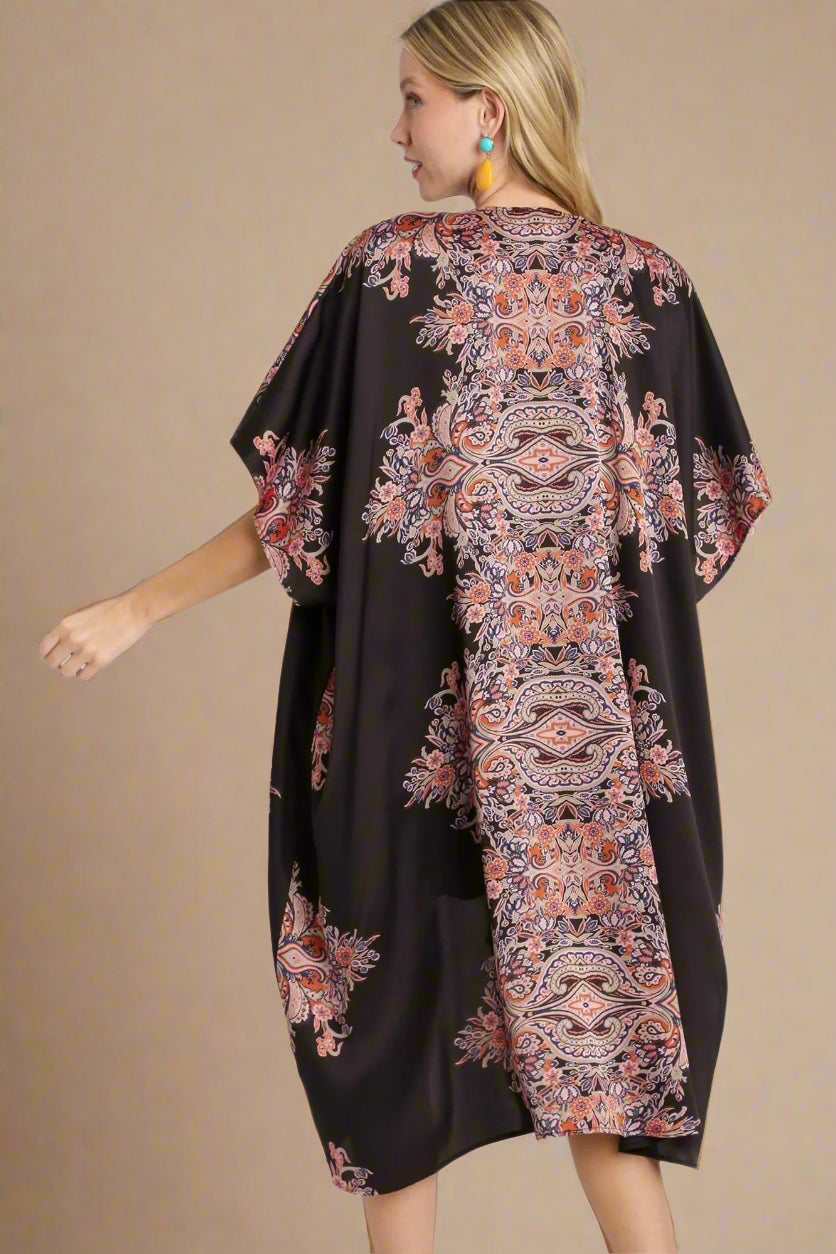 Woman wearing a black kimono-style dress with colorful floral patterns on a white background