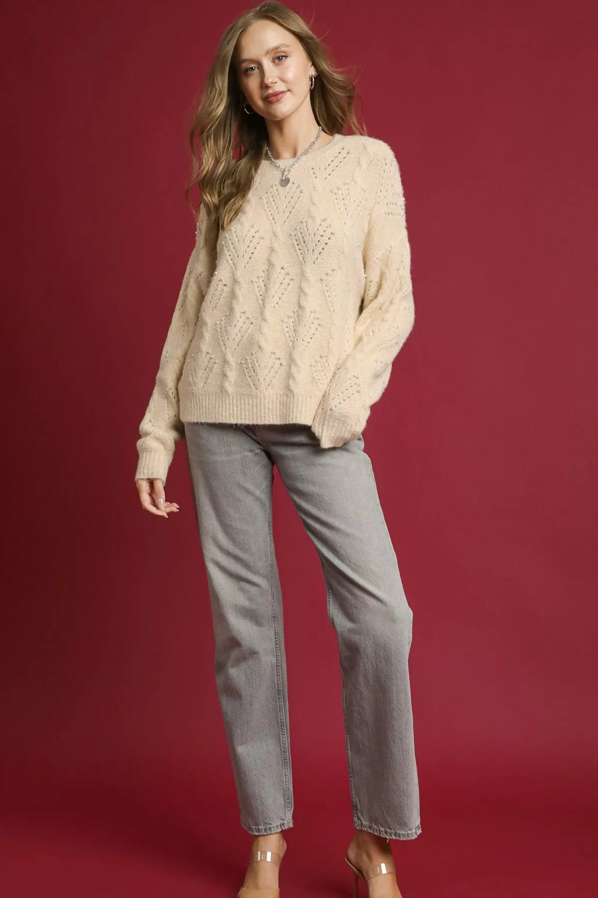 Woman wearing a cream sweater and gray jeans on a red background