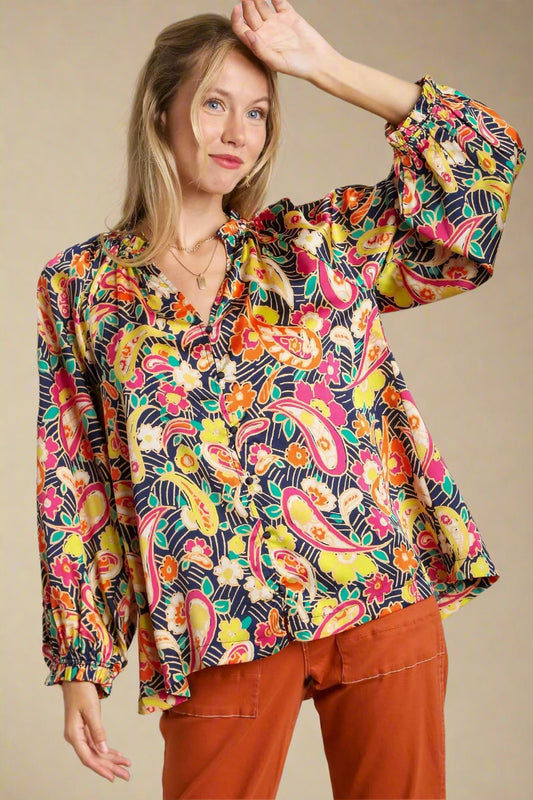 Woman wearing a colorful patterned blouse with orange pants against a neutral background