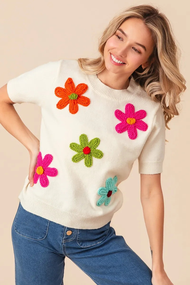 Woman wearing a white sweater with colorful flower appliqués on a beige background