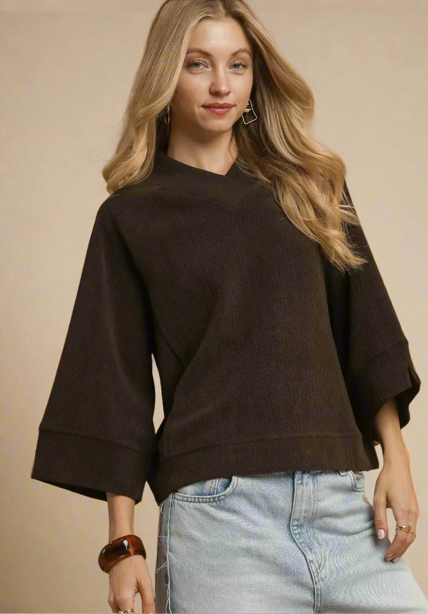 Woman wearing a brown sweater and light blue jeans against a beige background