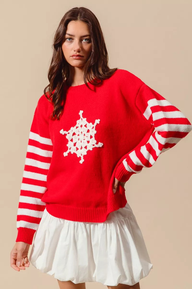 Woman wearing a red sweater with a white snowflake design and striped sleeves on a beige background