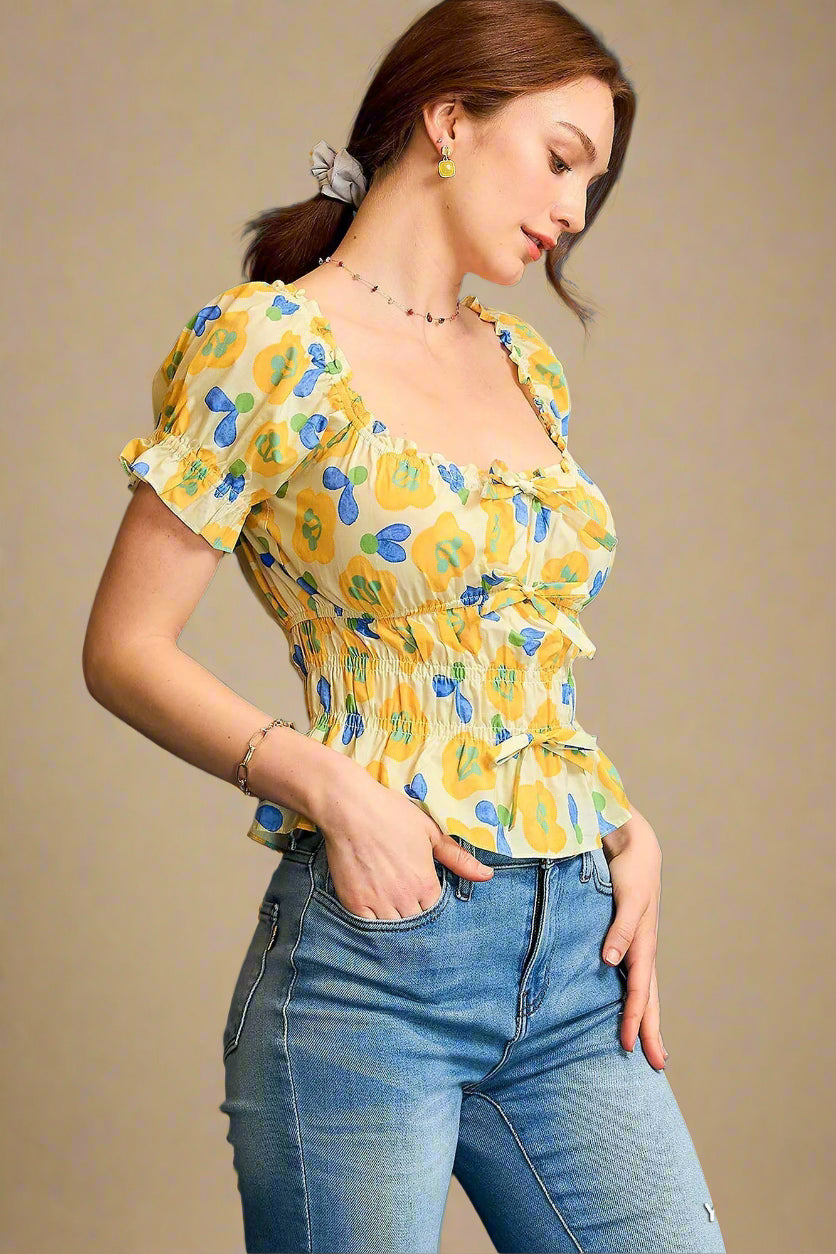Woman wearing a yellow floral top and blue jeans against a beige background