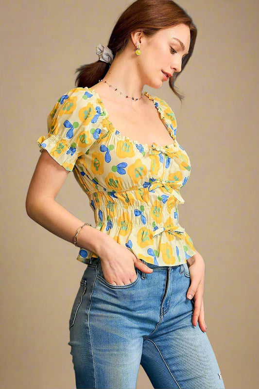 Woman wearing a yellow floral top and blue jeans against a beige background