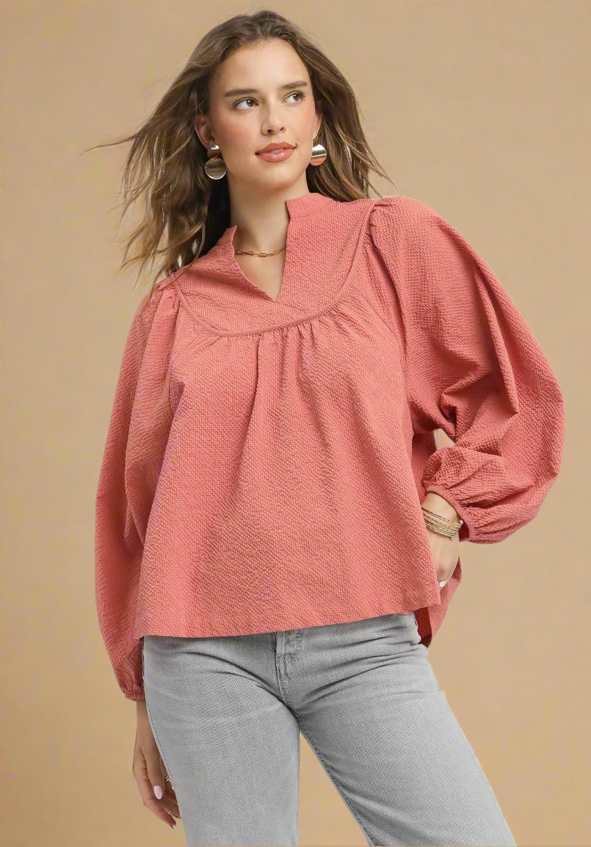 Woman wearing a dusty rose blouse and gray pants on a beige background