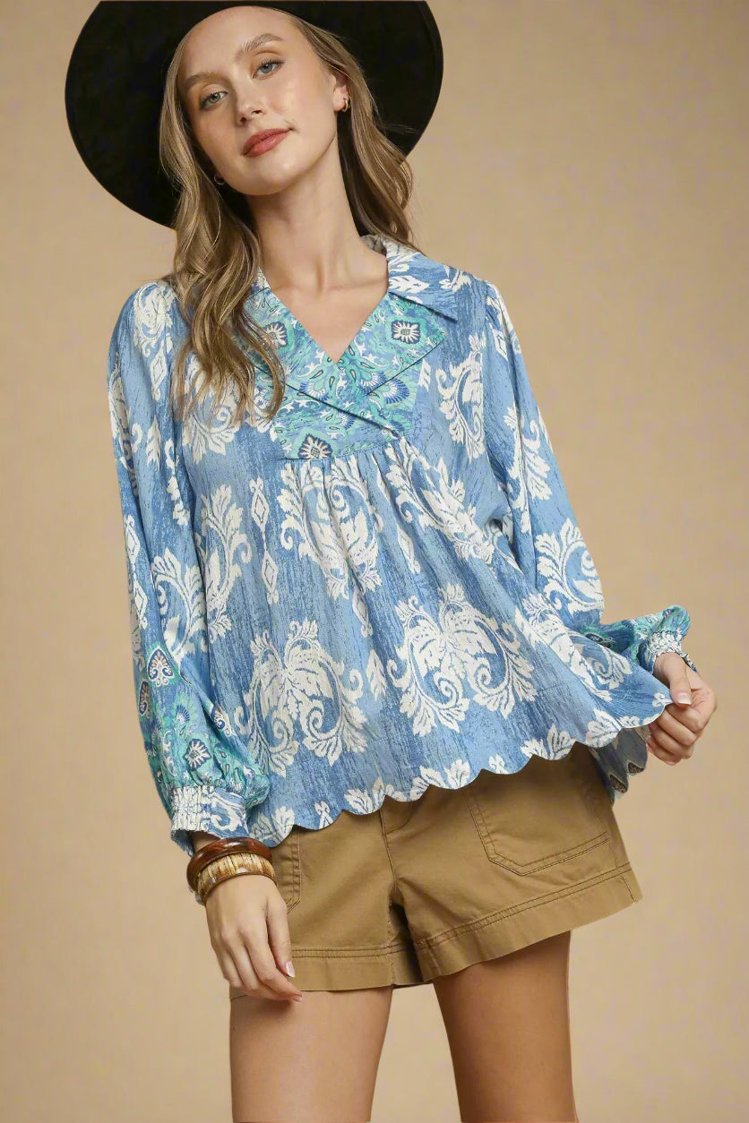 Woman wearing a blue patterned blouse and beige shorts against a beige background