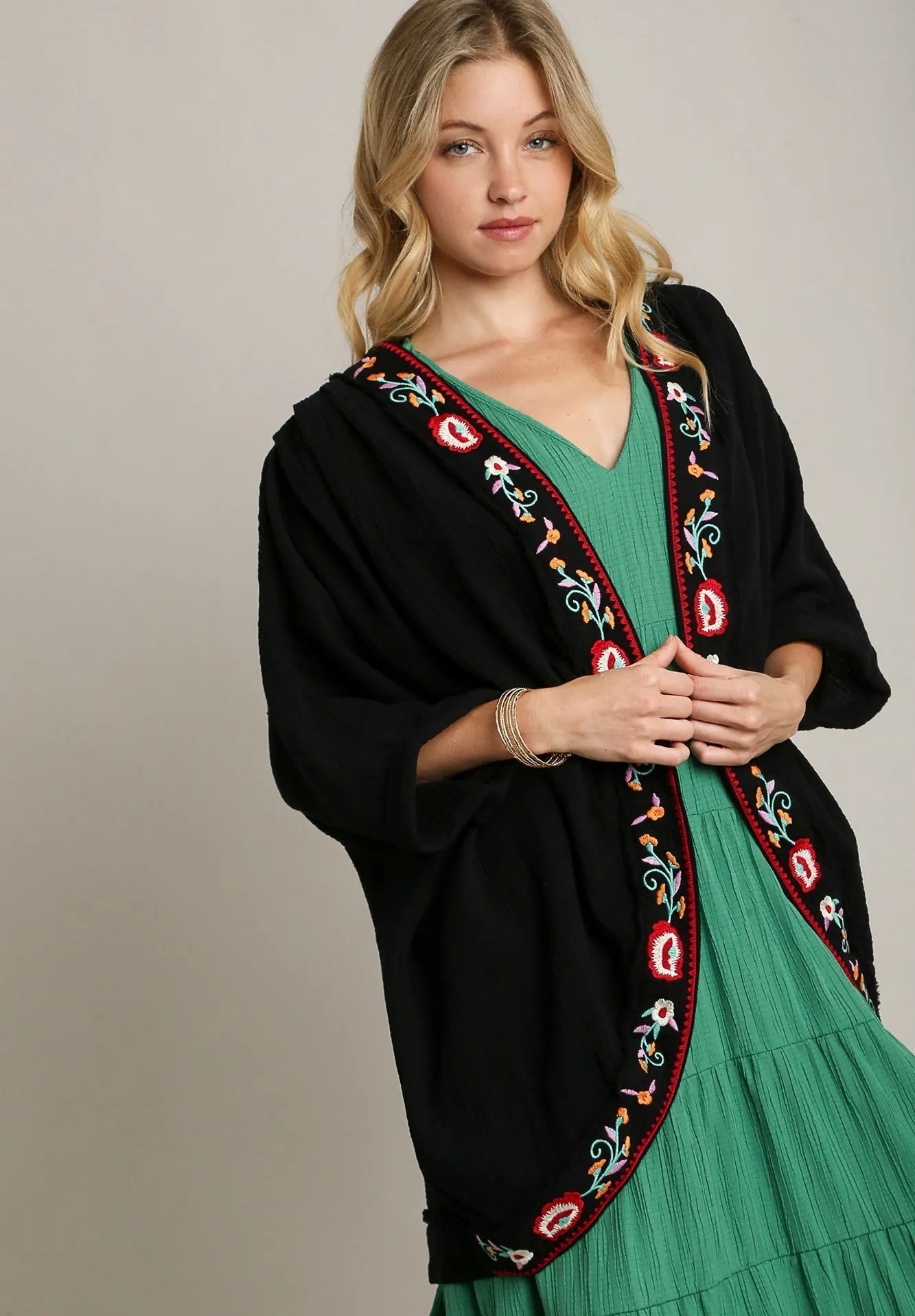 Woman wearing a black embroidered cardigan over a green dress on a beige background