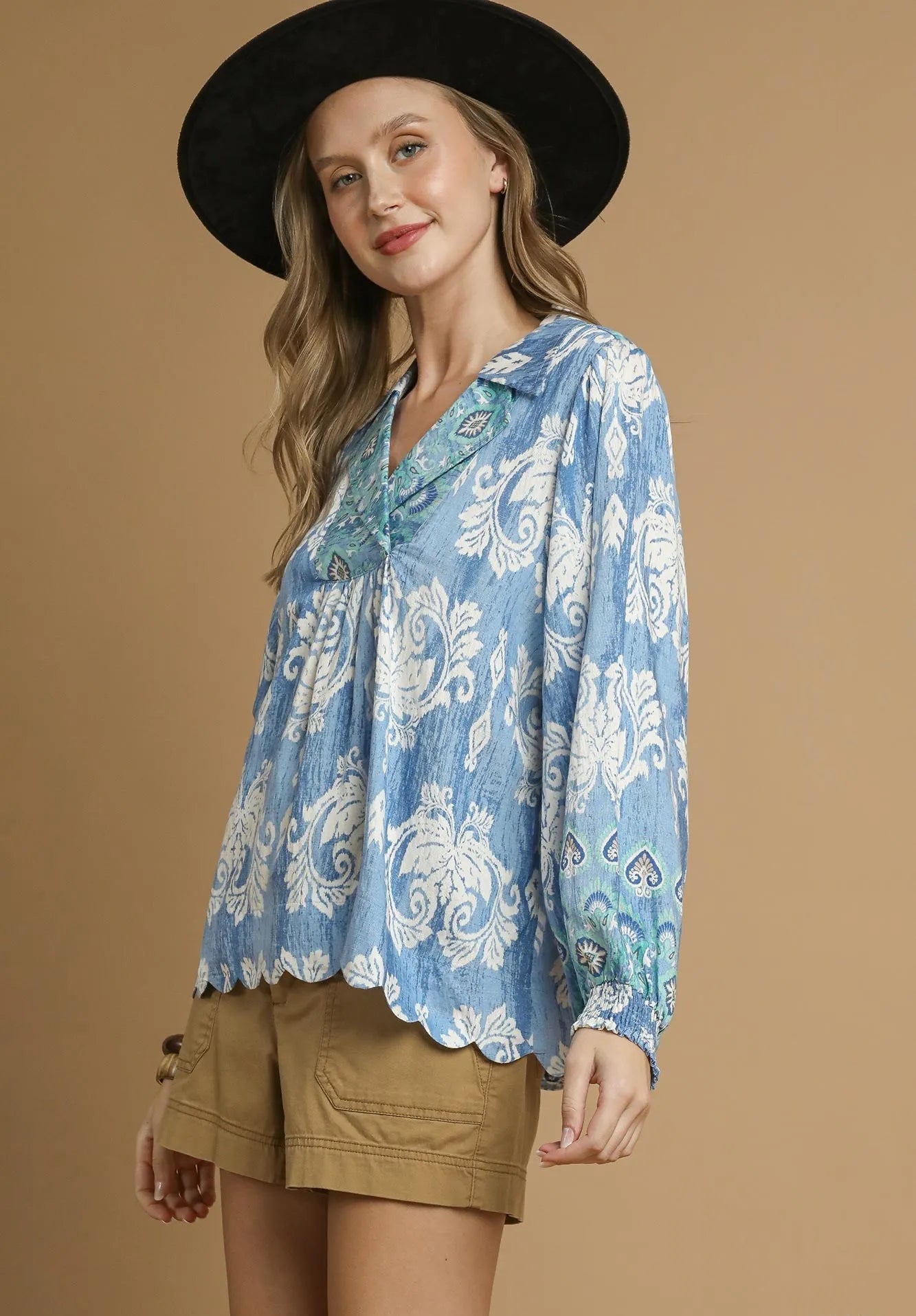 Woman wearing a blue floral blouse with a black hat on a beige background