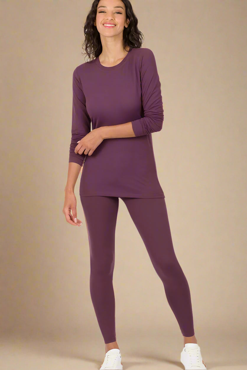 Woman wearing an eggplant-colored long-sleeve top and leggings on a beige background
