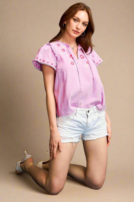 Woman wearing a pink blouse with floral patterns and white shorts on a beige background