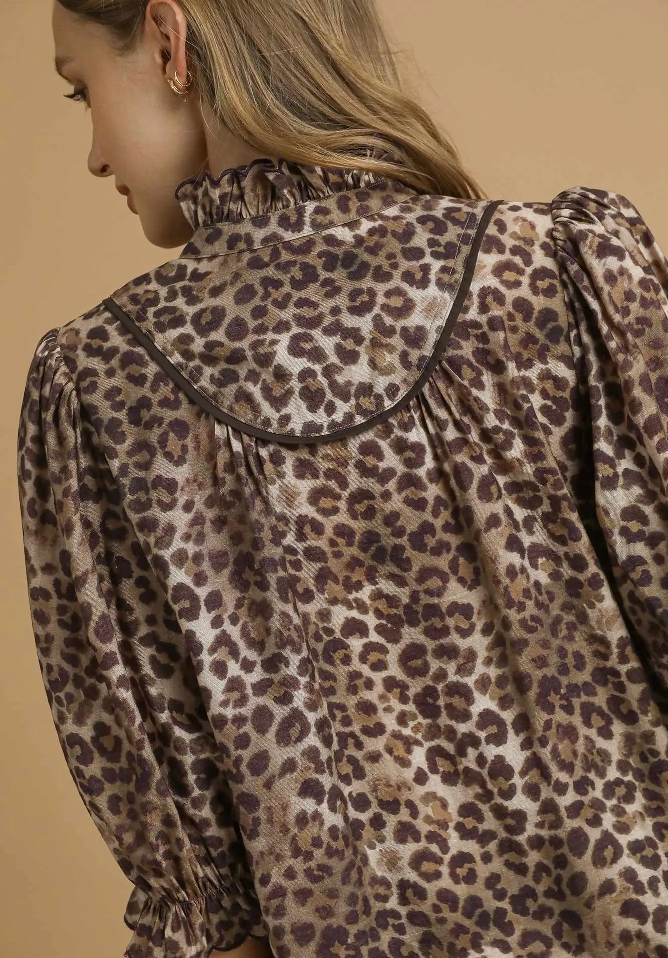Leopard print blouse worn by a person on a beige background