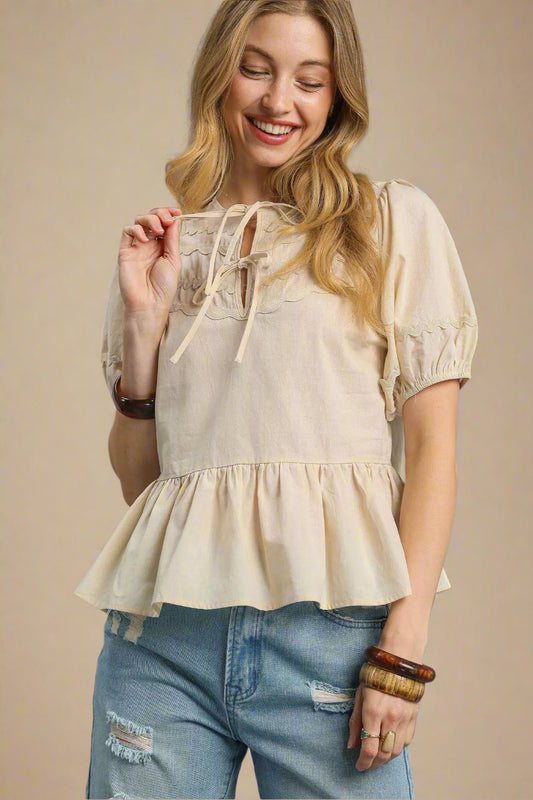 Woman wearing a beige blouse with lace details and blue jeans against a beige background