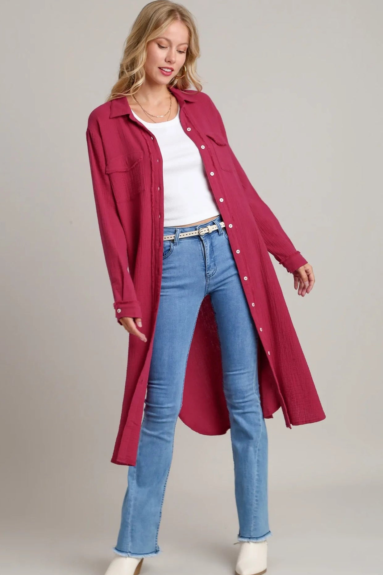 Woman wearing a long red coat over a white top and blue jeans on a plain background