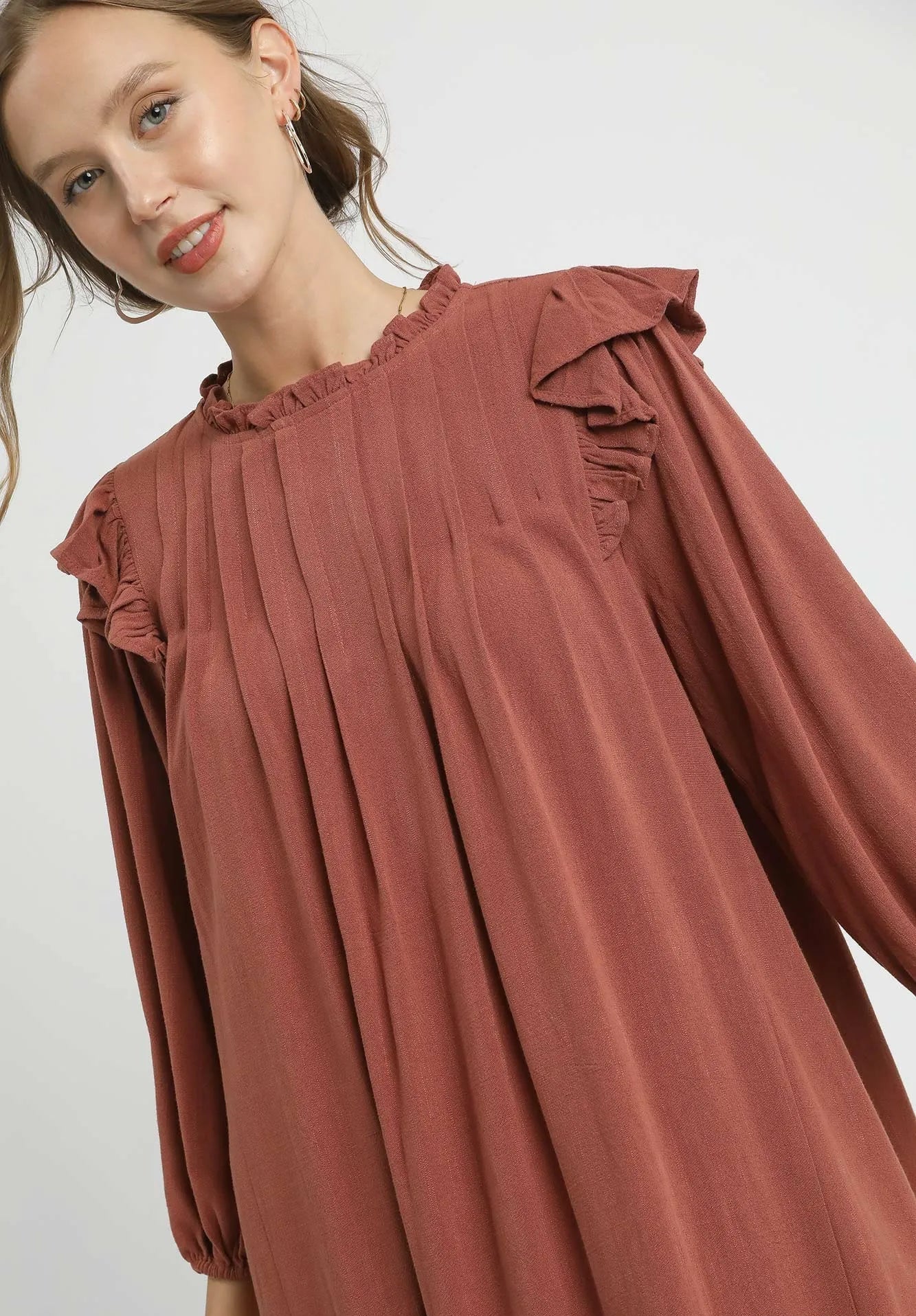 Woman wearing a rust-colored dress with ruffled shoulders on a white background