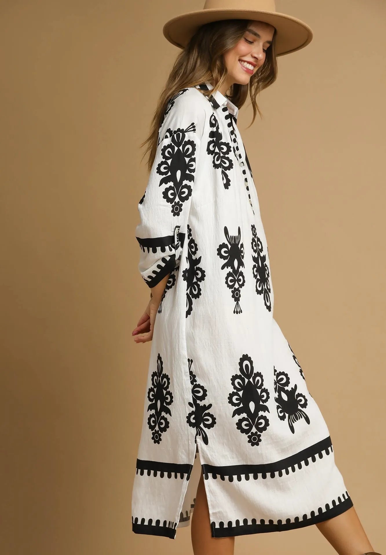 Woman wearing a white dress with black patterns and a beige hat on a beige background