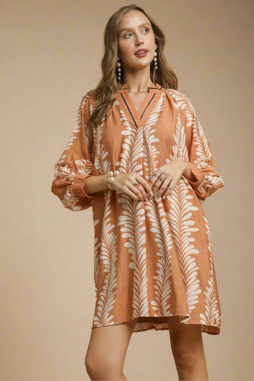 Woman wearing a taupe dress with leaf pattern on a beige background