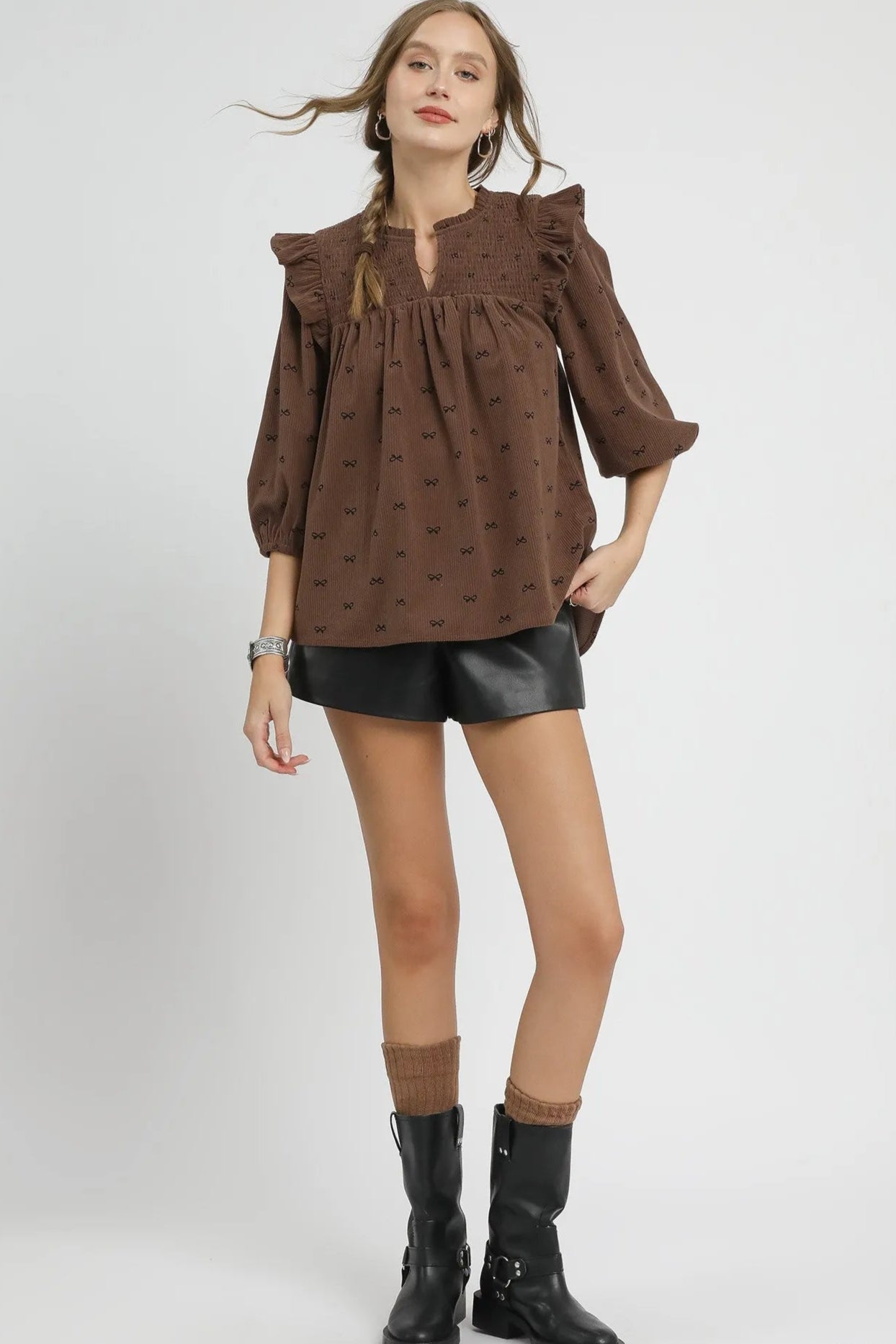 Woman wearing a brown blouse with ruffled sleeves and black shorts on a white background