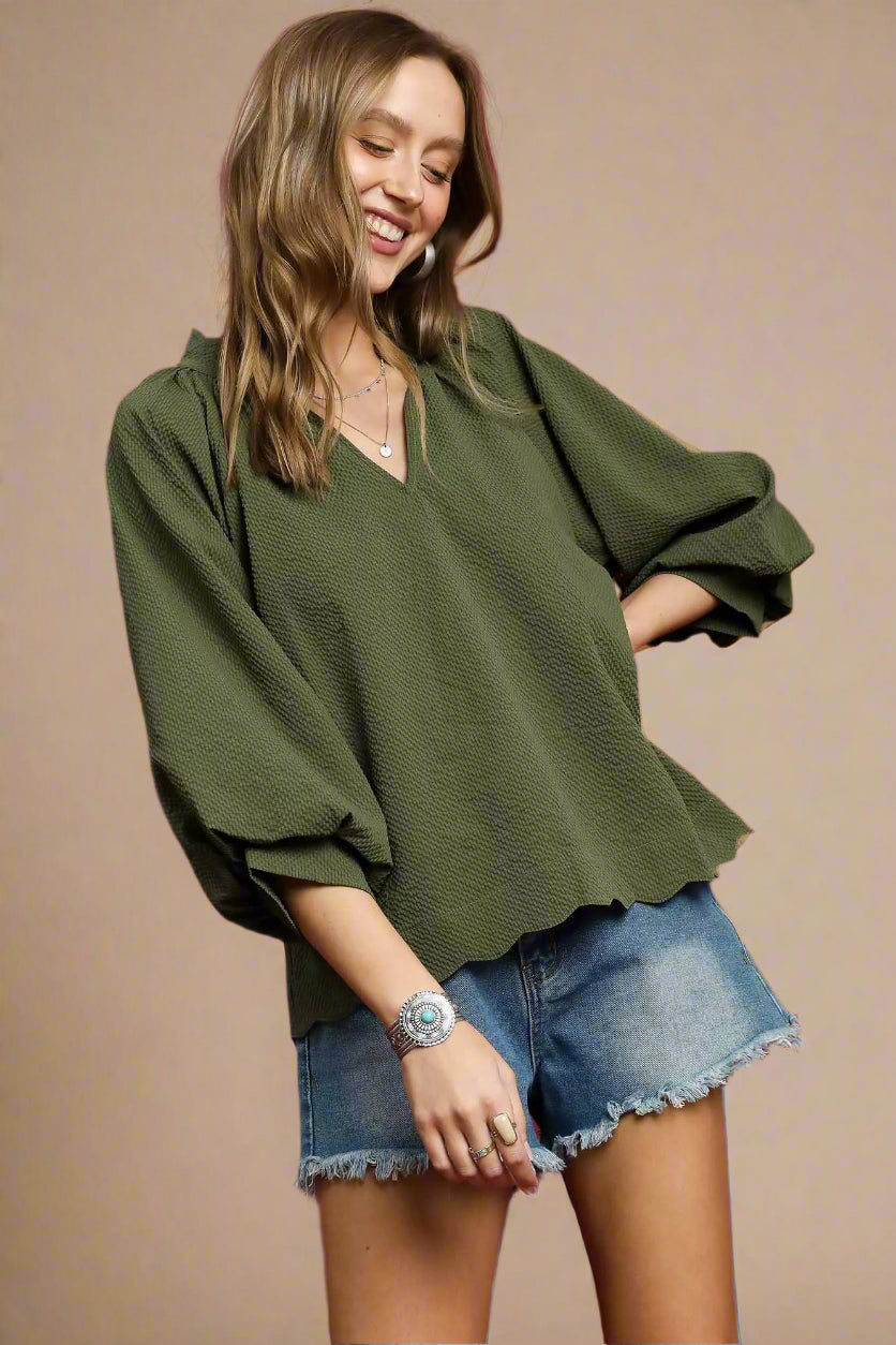 Woman wearing an olive green top and denim shorts on a red background