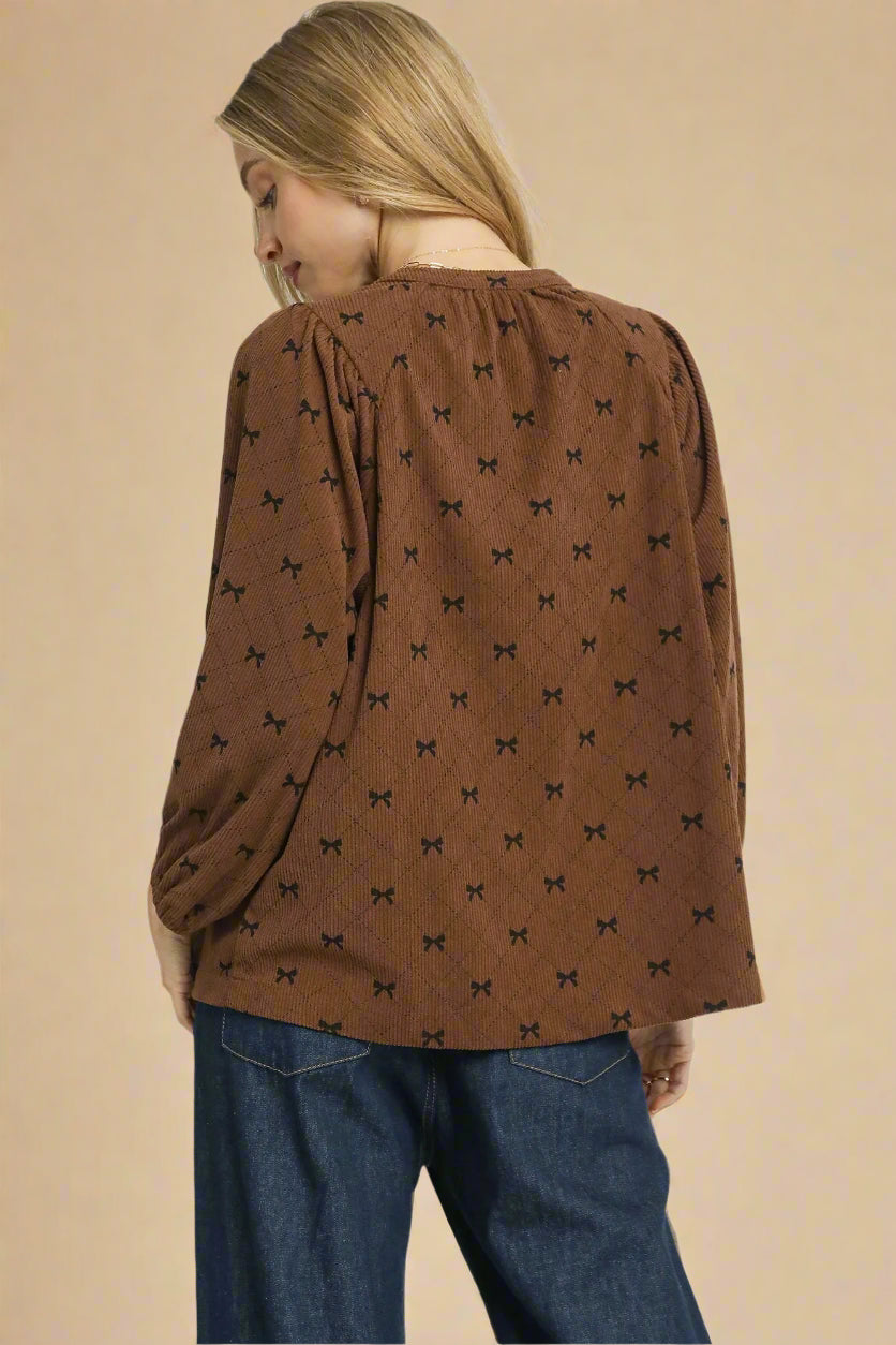 Woman wearing a brown blouse with black patterns and blue jeans on a beige background