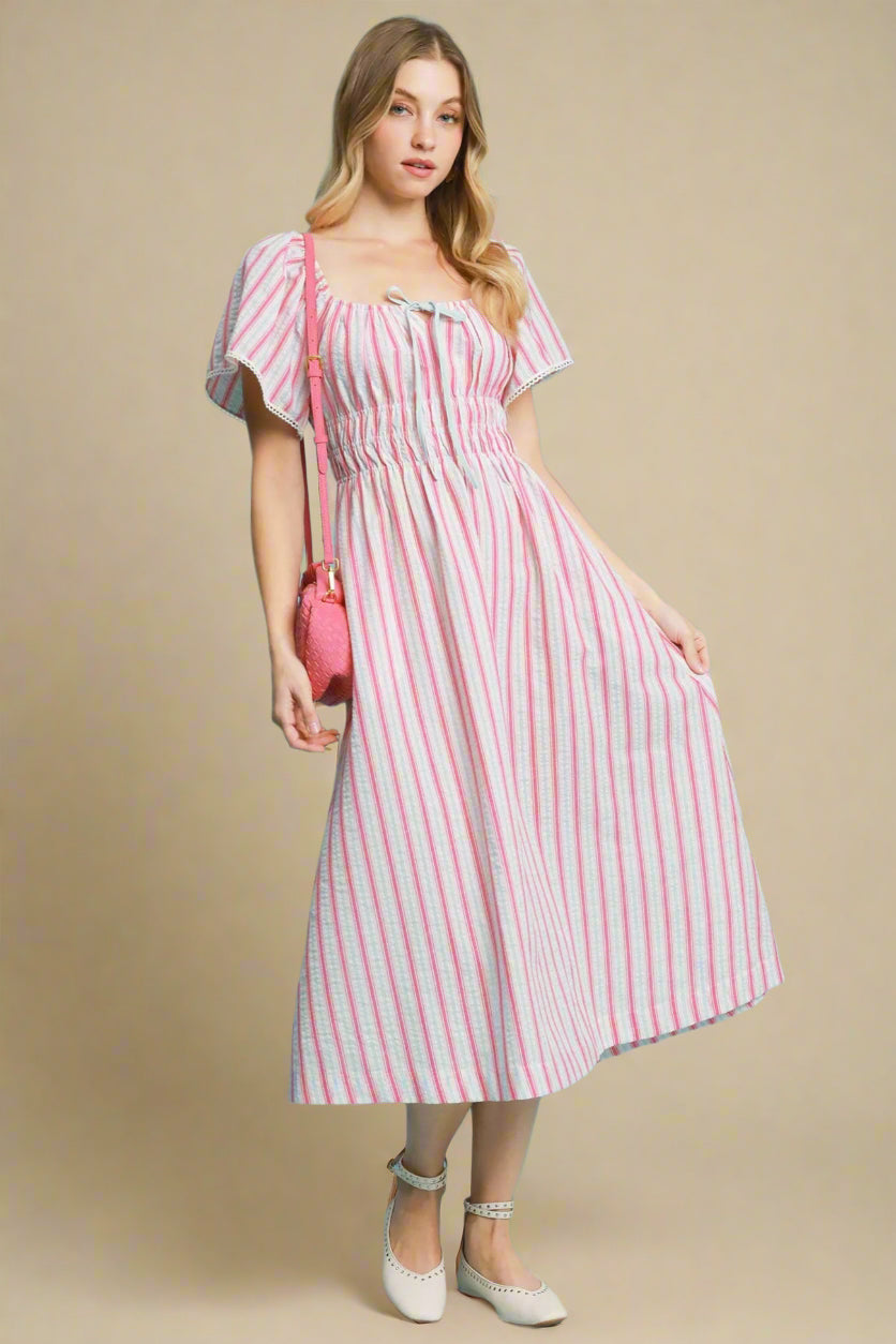 Woman wearing a pink and blue striped dress against a beige background