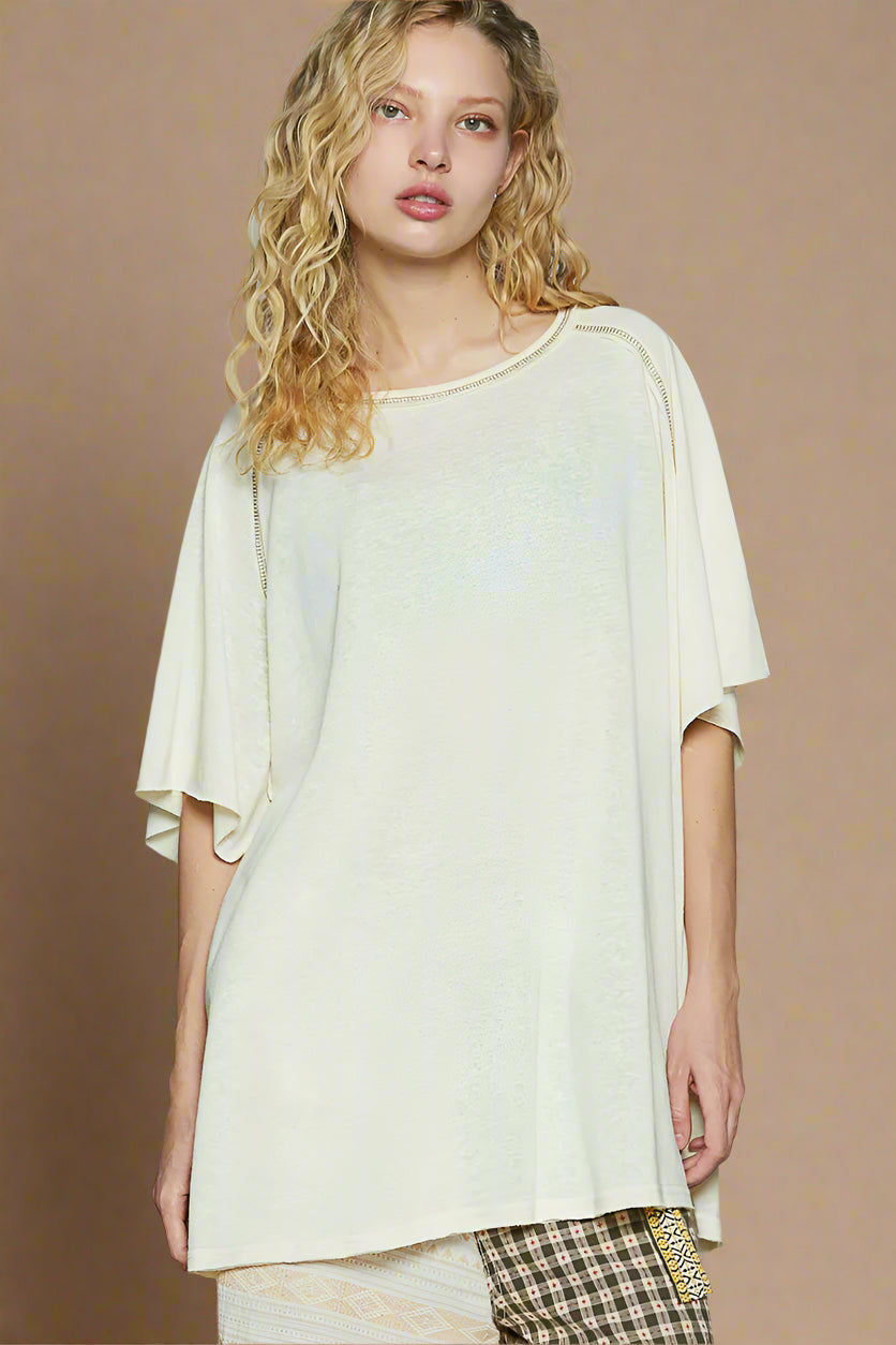 Woman wearing a light-colored oversized top with a plain background