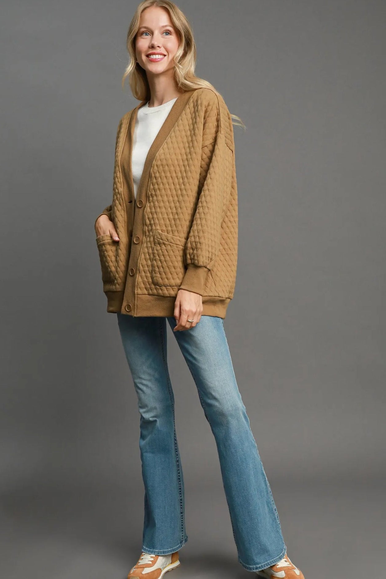 Woman wearing a brown quilted jacket and blue jeans on a gray background