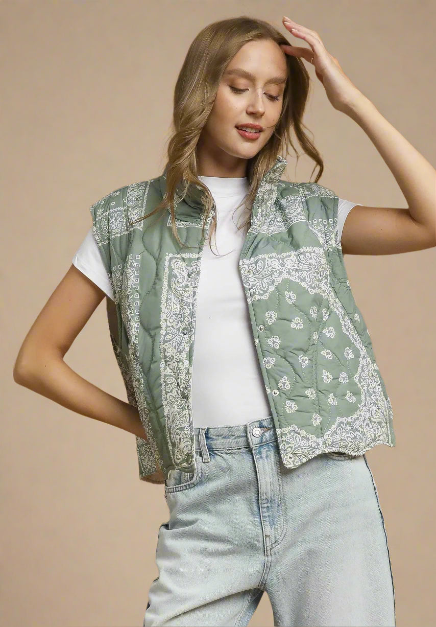 Woman wearing a green patterned vest over a white shirt and light blue jeans on a beige background