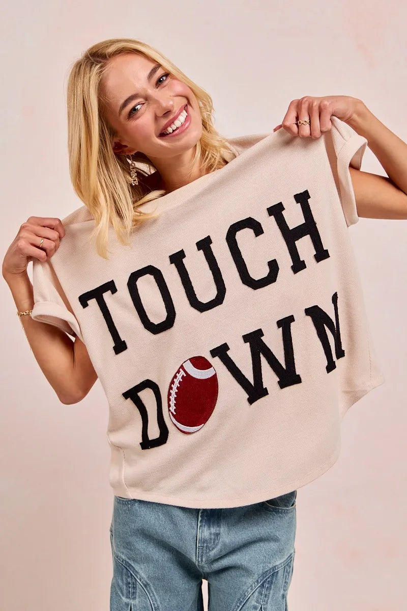 Woman wearing a beige oversized t-shirt with 'TOUCHDOWN' and a football graphic.