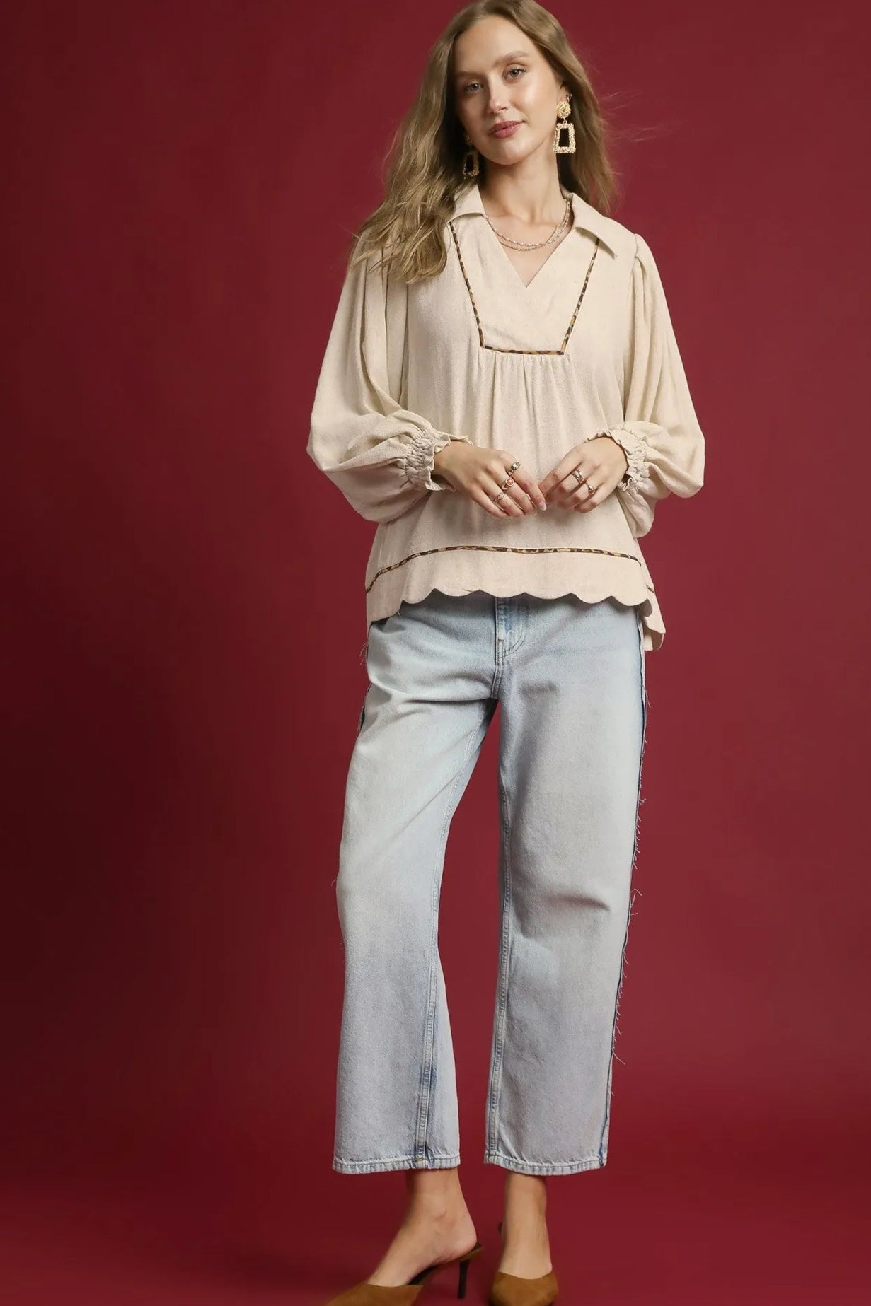 Woman wearing a beige blouse and light blue jeans against a red background