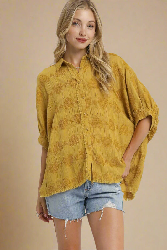 Woman wearing a mustard yellow patterned shirt and denim shorts on a beige background