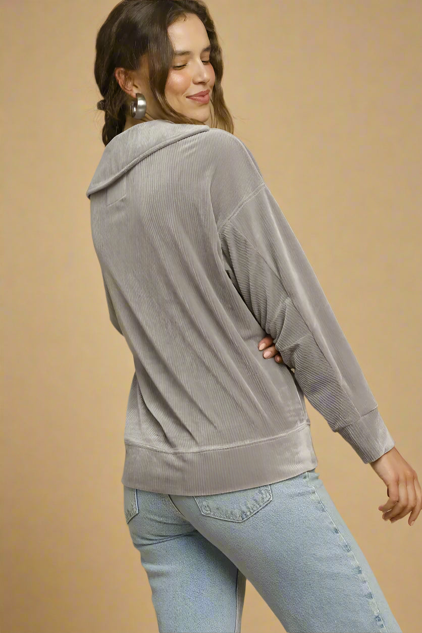 Woman wearing a gray top and light blue jeans against a beige background