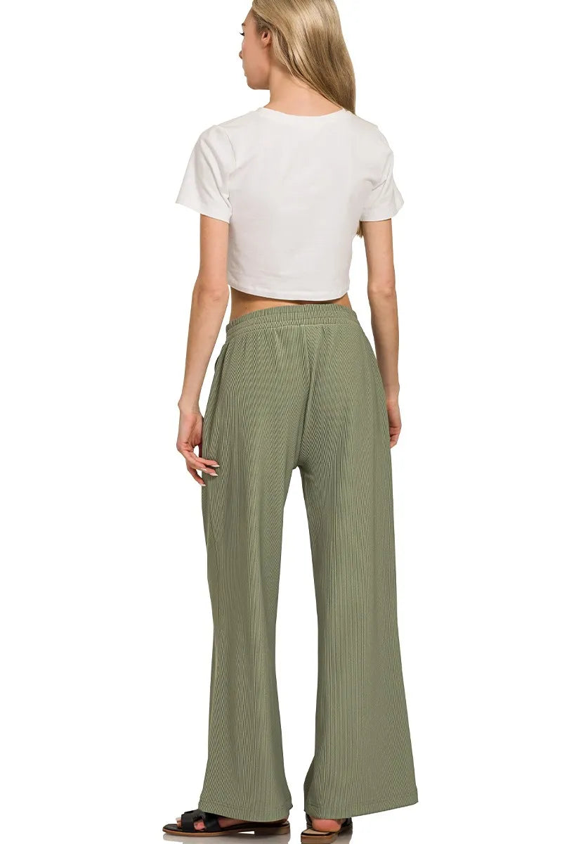 Woman wearing a white crop top and green wide-leg pants on a white background