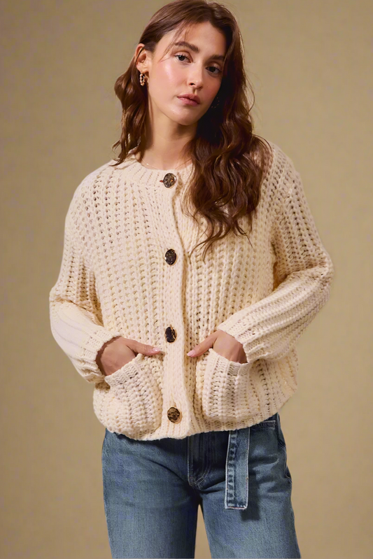 Woman wearing a beige knitted cardigan with button details on a beige background