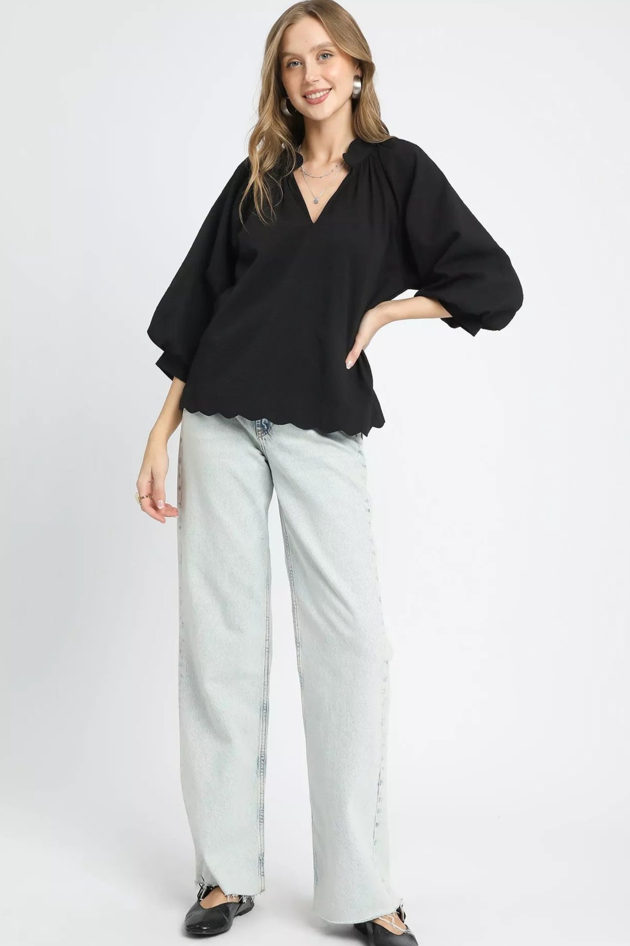 Woman wearing a black blouse and light gray pants on a white background