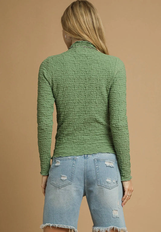 Person wearing a green textured sweater and denim shorts on a beige background