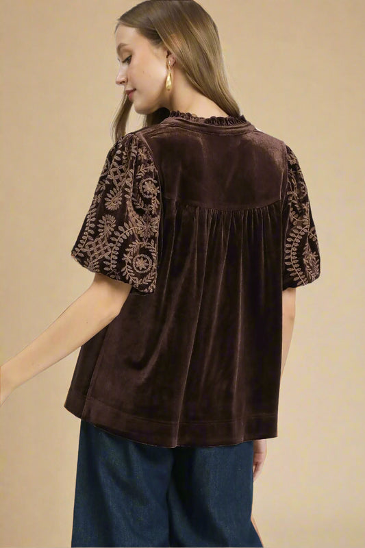 Woman wearing a brown velvet blouse with lace sleeves on a gray background