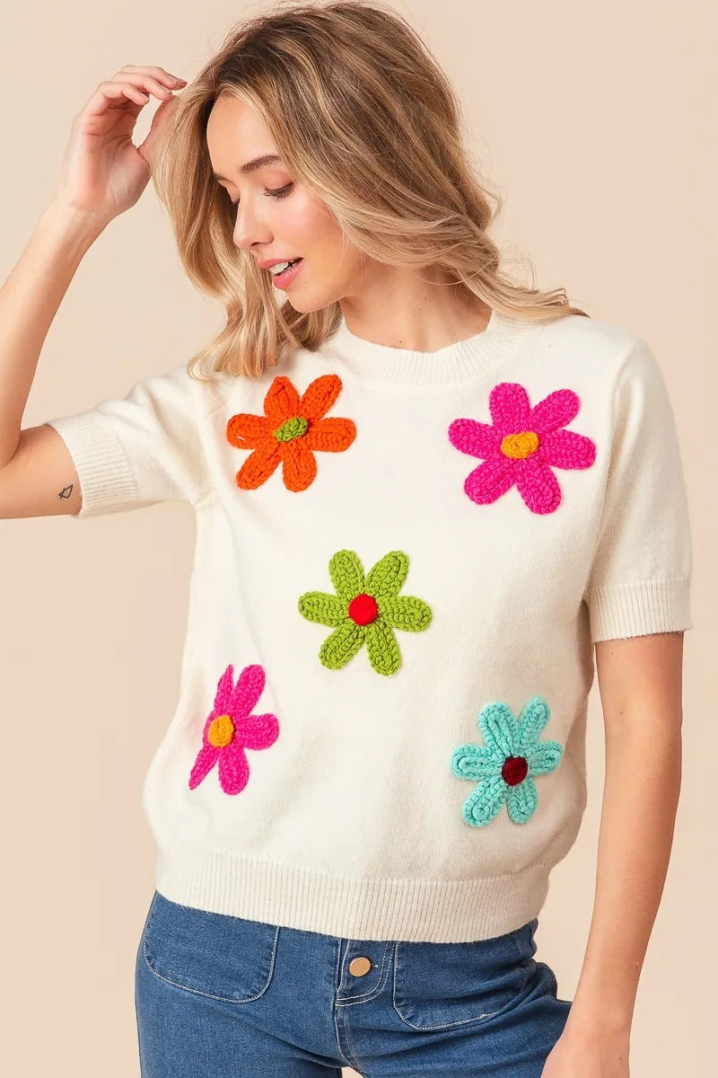 Woman wearing a cream sweater with colorful flower patterns on a beige background