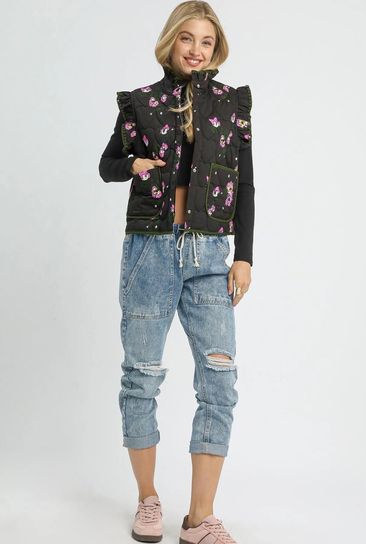 Woman wearing a black floral jacket and blue jeans on a white background
