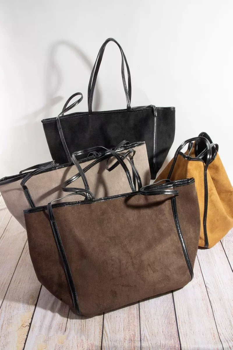 Three handbags in black, brown, and yellow on a wooden surface with a white background