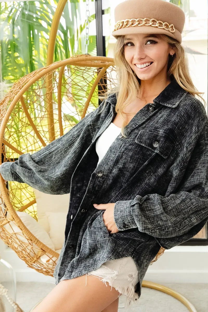 Woman wearing a denim jacket and beige hat sitting in a wicker chair with greenery in the background
