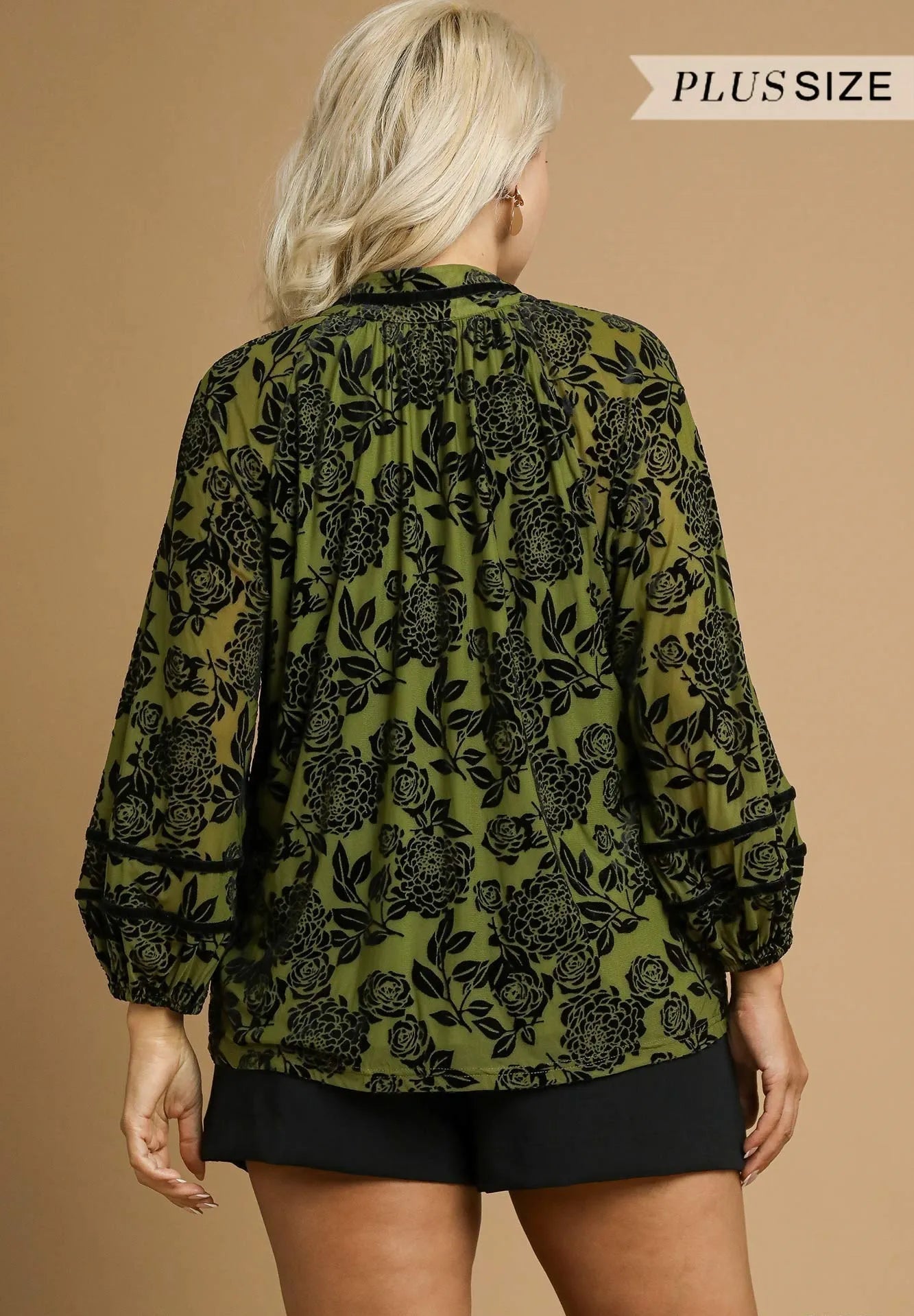 Woman wearing a green floral blouse with black patterns on a beige background