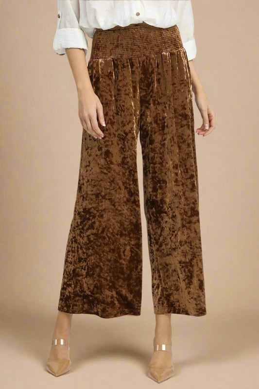 Brown crushed velvet wide-leg pants worn by a person on a beige background