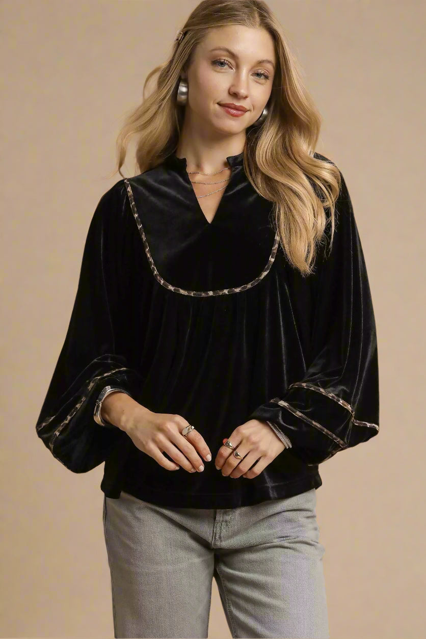 Woman wearing a black velvet blouse with decorative trim on a beige background