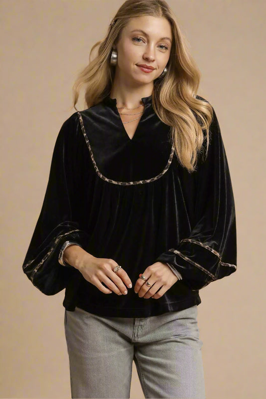 Woman wearing a black velvet blouse with decorative trim on a beige background