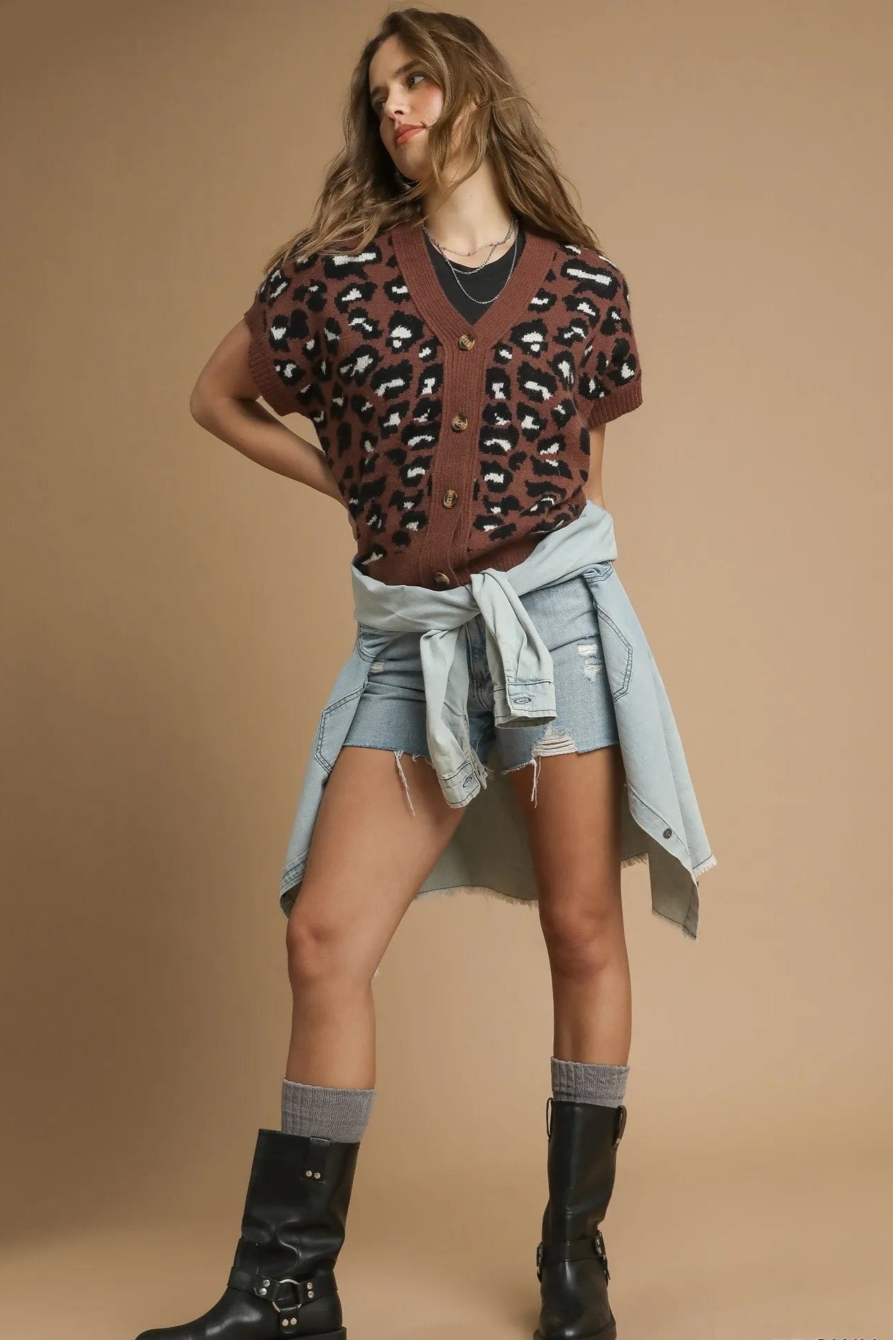 Woman wearing a patterned brown top, gray skirt, and black boots on a beige background