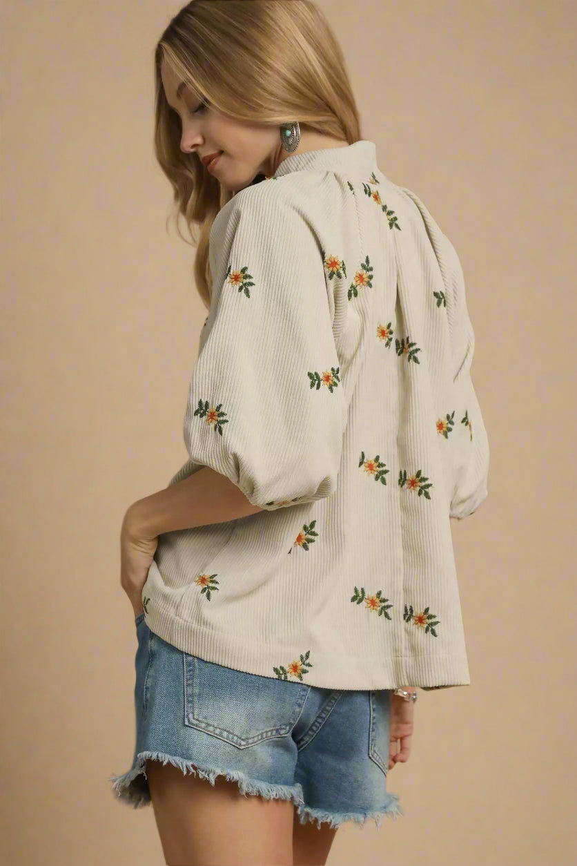 Woman wearing a cream-colored blouse with floral patterns and denim shorts on a beige background