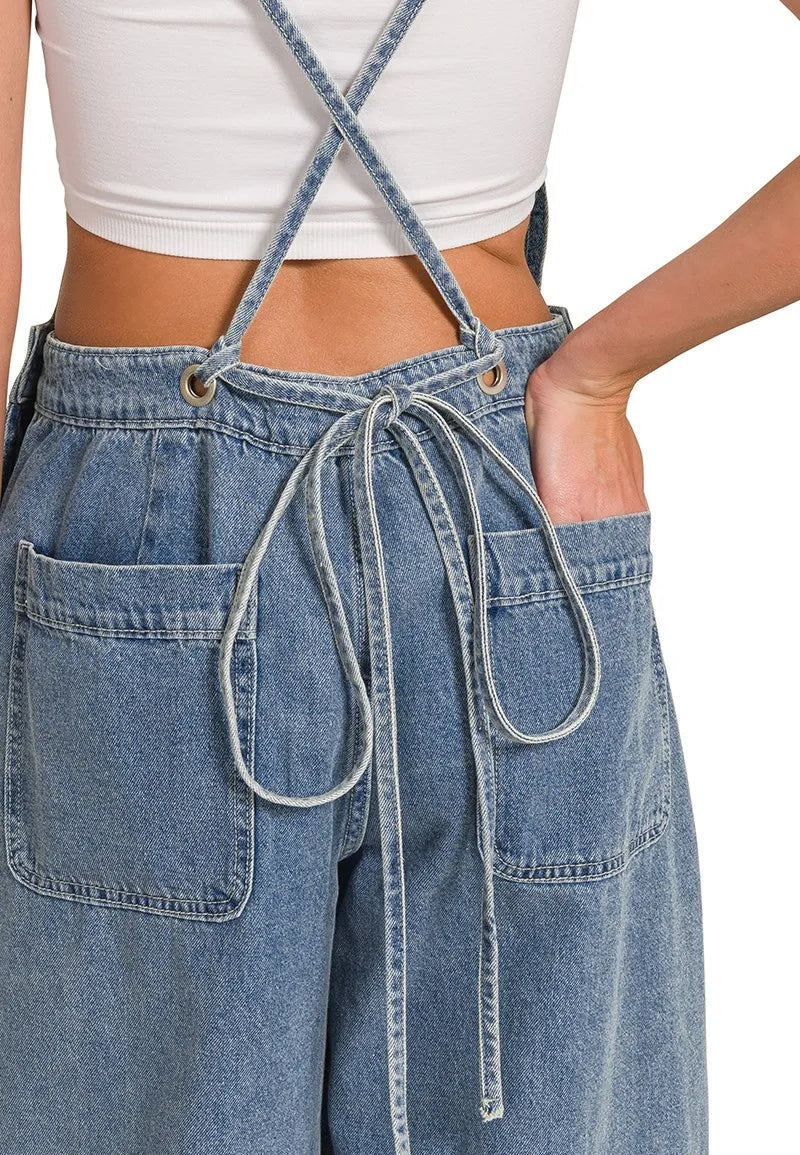 Blue denim wide-leg pants with thin straps worn by a person, on a plain background.