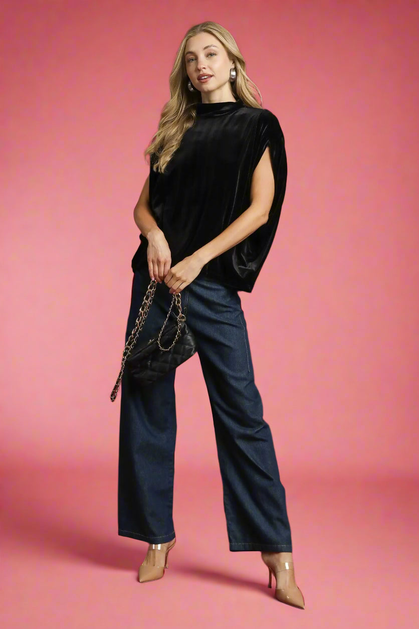 Woman in black top and blue pants holding a black handbag against a red background