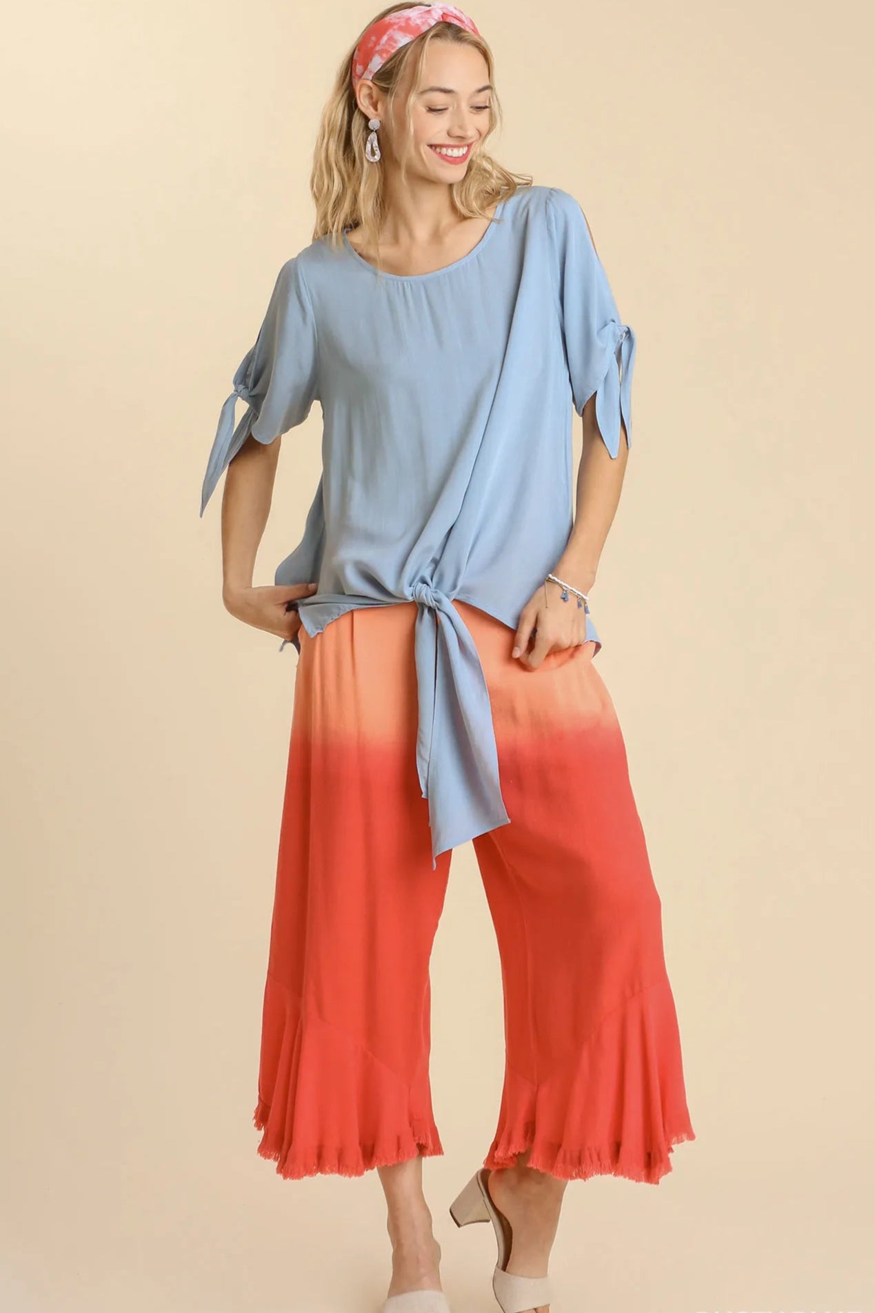 Woman wearing a blue top and red-orange pants on a beige background